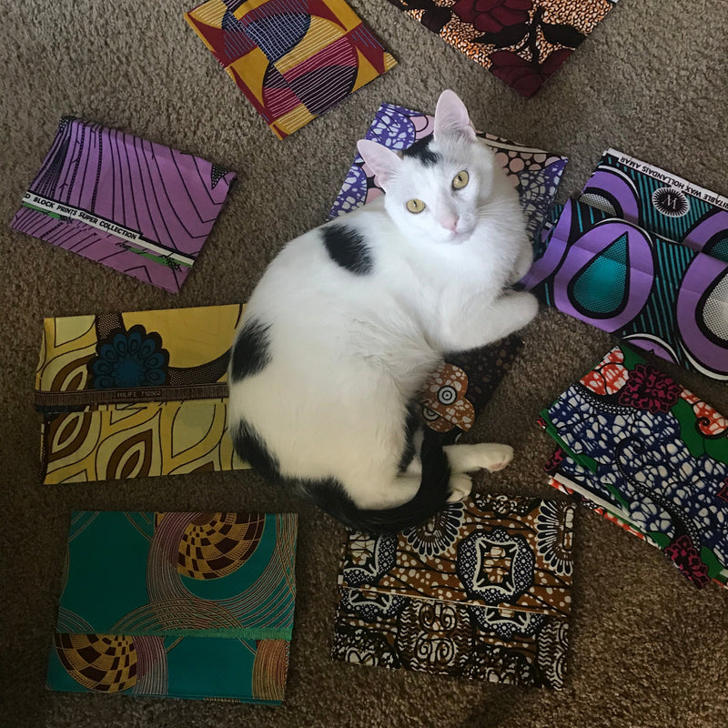 Cat sitting on a colorful patterned box with more boxes around on a brown carpet